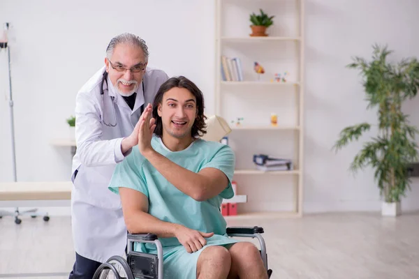 Junger männlicher Patient im Rollstuhl und erfahrener Arzt Traumatologe — Stockfoto