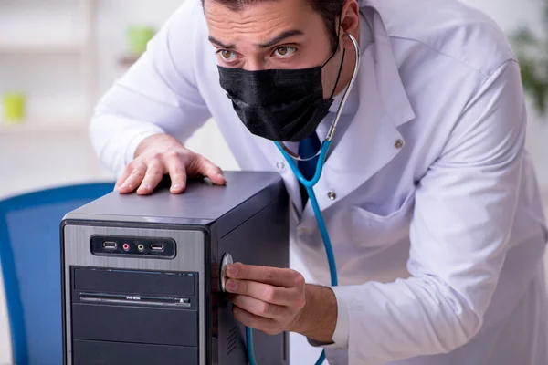 Joven doctor masculino con estetoscopio reparando computadora —  Fotos de Stock