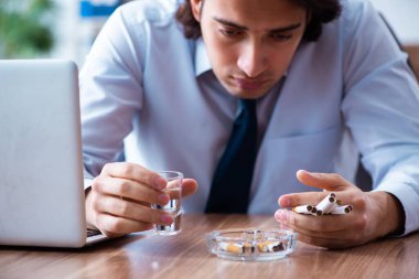 İş yerinde votka içip sigara içen bir erkek işçi.