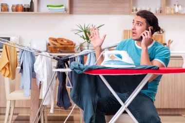 Genç adam evde çamaşır ütülüyor.