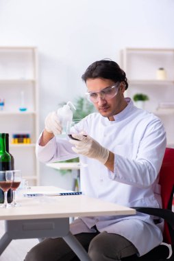Erkek kimyager laboratuvarda şarap örneklerini inceliyor.
