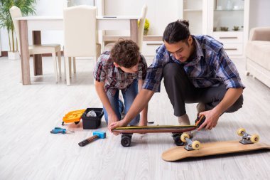 Genç baba oğluyla kaykay tamir ediyor.