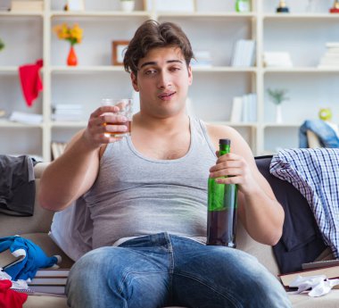 Dağınık bir odada alkol alan genç bir öğrenci.