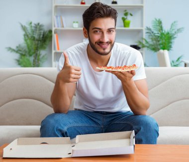 Pizza yiyen adam evde yemek yiyor, dinleniyor.