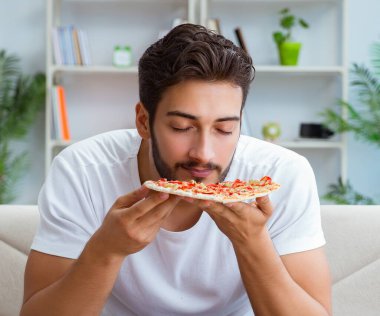 Pizza yiyen adam evde yemek yiyor, dinleniyor.