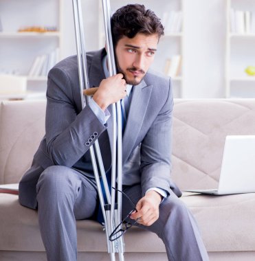 Koltuk değneği ve kırık bacağı olan bir iş adamı.