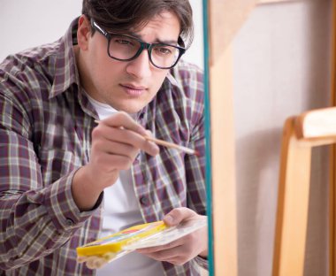 Genç erkek sanatçı parlak stüdyoda resimler çiziyor.