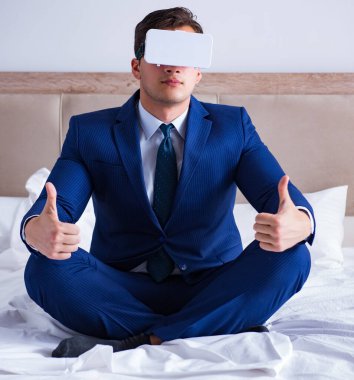 Yatak odasında sanal gerçeklik kulaklığı takan bir iş adamı.