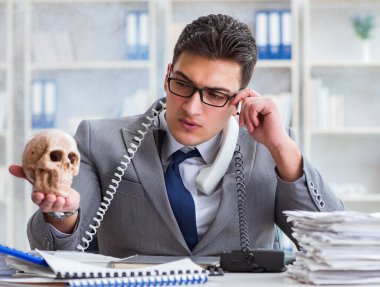 Ofisteki işadamı elinde insan kafatasıyla sigara içiyor.