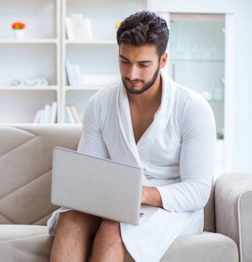 Genç adam evde dizüstü bilgisayarla çalışıyor.