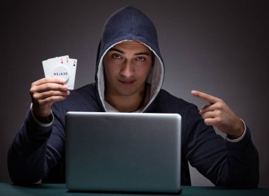 Kapüşonlu genç adam dizüstü bilgisayarın önünde oturuyor.