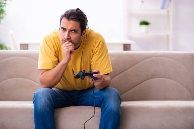 Genç adam evde joystick oynuyor.