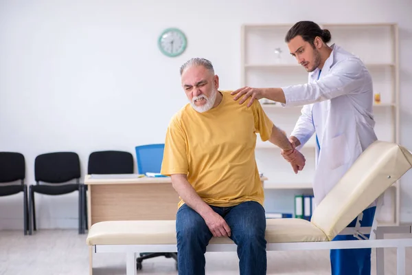 Vecchio ferito visitando giovane medico chiropratico maschile — Foto Stock