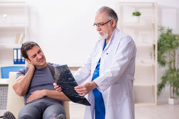 Jeune athlète masculin visitant un vieux médecin radiologue — Photo