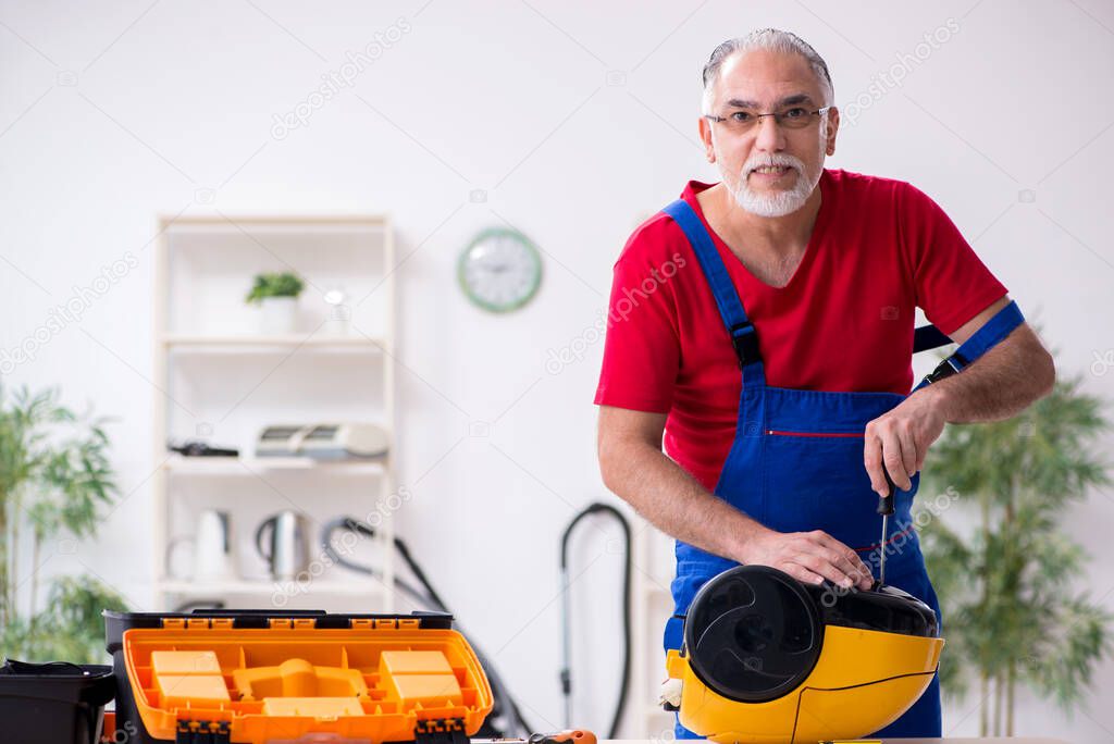 Old male contractor repairing vacuum cleaner indoors