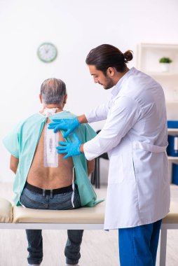 Yaşlı adam genç erkek doktoru ziyaret ediyor.