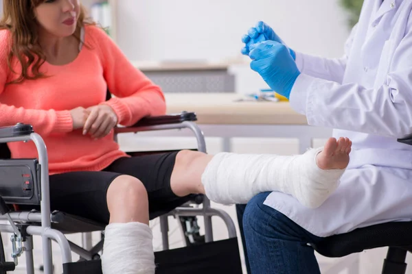 Jonge been gewonde vrouw op bezoek bij oude arts traumatoloog — Stockfoto