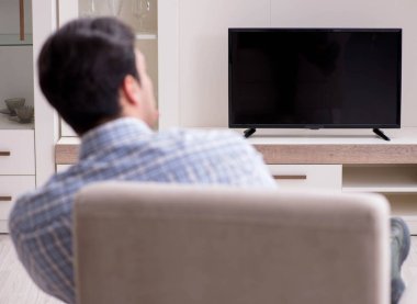 Genç adam evde televizyon izliyor.