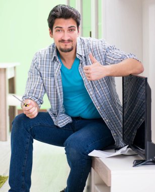 Genç adam evde televizyon tamir ediyor.