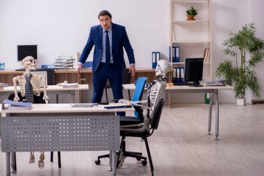 Ofiste iskeletleri olan genç bir erkek çalışan.
