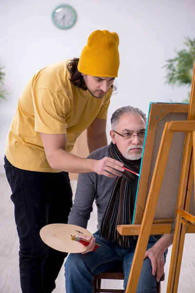 Old man taking lesson from young painter