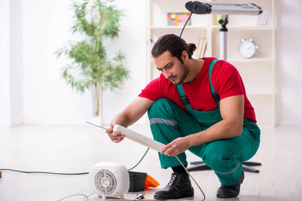 Jovem empreiteiro masculino reparando aquecedor de ventilador dentro de casa — Fotografia de Stock