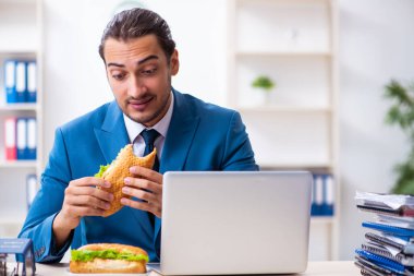 Genç erkek çalışan işyerinde kahvaltı yapıyor.