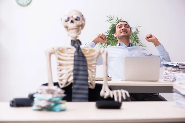 Młody mężczyzna pracownik i szkielet w biurze — Zdjęcie stockowe