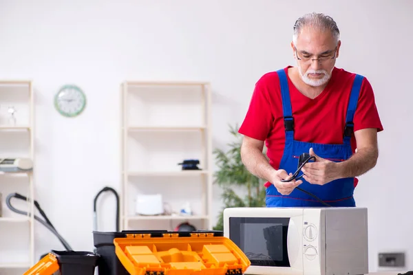 Empreiteiro velho do sexo masculino reparar microondas dentro de casa — Fotografia de Stock