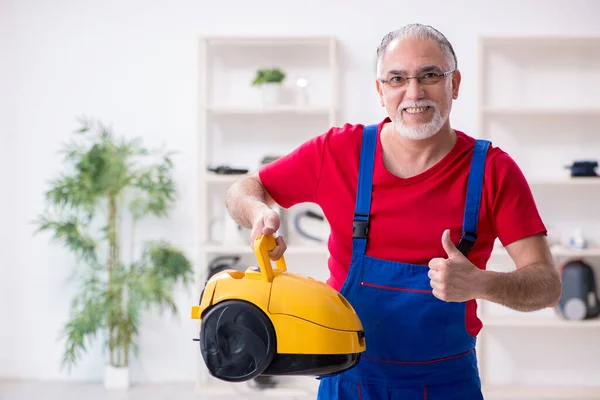 Old male contractor repairing vacuum cleaner indoors