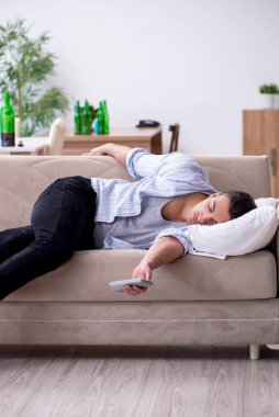Genç erkek alkolik partiden sonra televizyon izliyor.