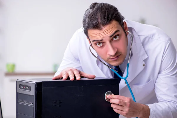 Joven doctor masculino con estetoscopio reparando computadora —  Fotos de Stock