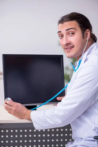 Joven doctor masculino con estetoscopio reparando computadora —  Fotos de Stock