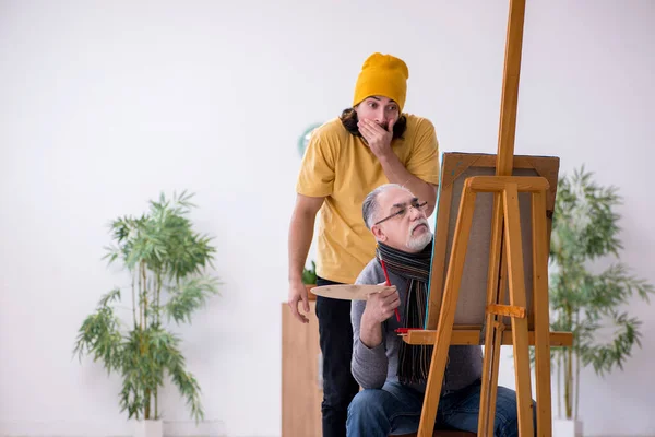 Old man taking lesson from young painter