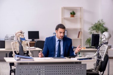 Ofiste iskeletleri olan genç bir erkek çalışan.