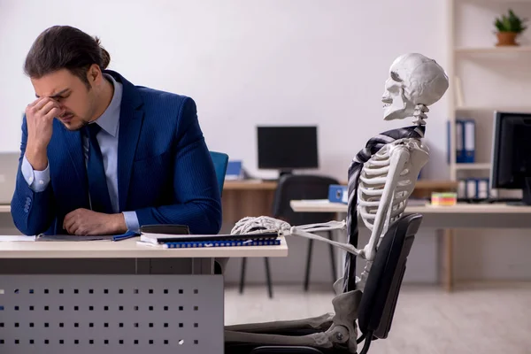 Young male employee with skeletons in the office — Stock Photo, Image