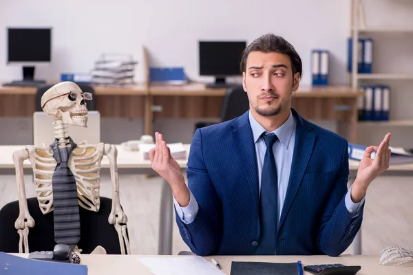 Молодой работник со скелетами в офисе — стоковое фото