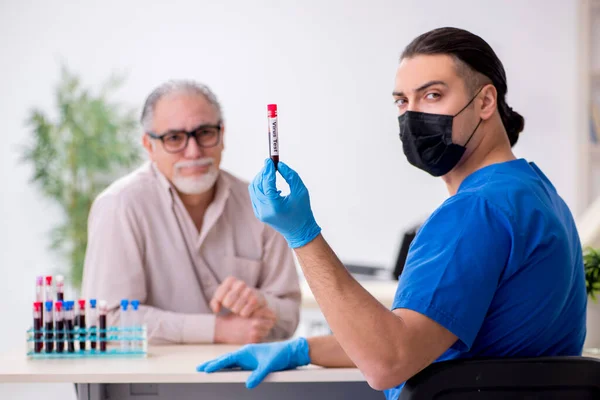 Velho paciente visitando jovem médico do sexo masculino no conceito de amostragem de sangue — Fotografia de Stock