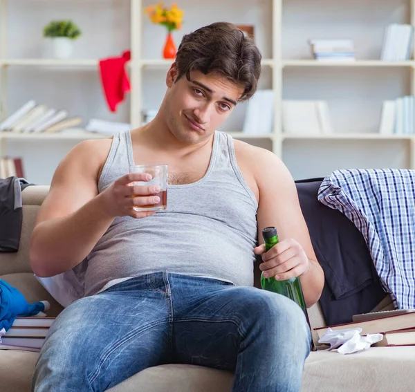 Dağınık bir odada alkol alan sarhoş genç adam.