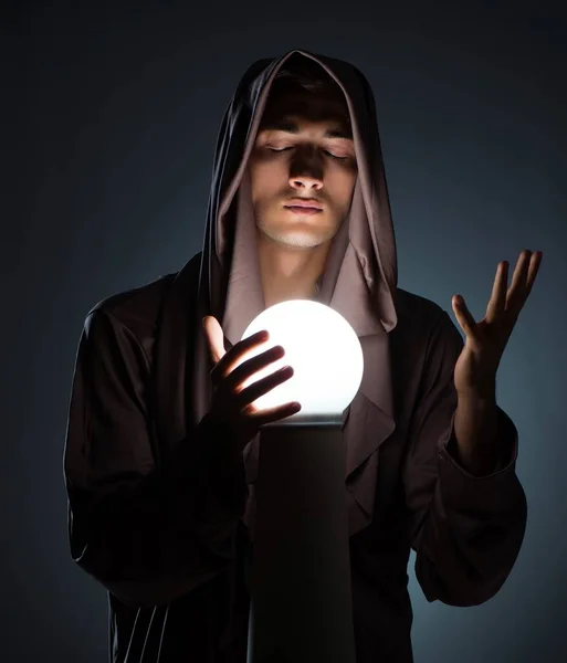 Молодий чарівник з кришталевим м'ячем у темній кімнаті — стокове фото