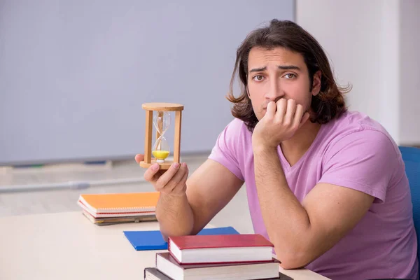 Jonge mannelijke student in het klaslokaal op tijdmanagementconcept — Stockfoto