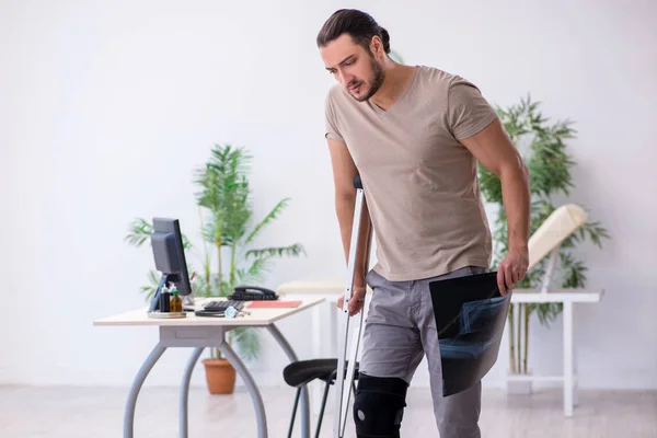 Jovem perna ferido homem com muletas olhando raio-x — Fotografia de Stock