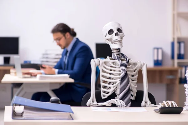 Young male employee with skeletons in the office — Stock Photo, Image