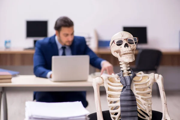 Young male employee with skeletons in the office — Stock Photo, Image