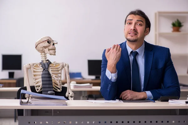 Молодой работник со скелетами в офисе — стоковое фото