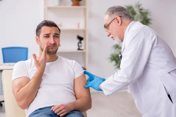 Mladý muž na návštěvě zkušeného lékaře dermatolog — Stock fotografie