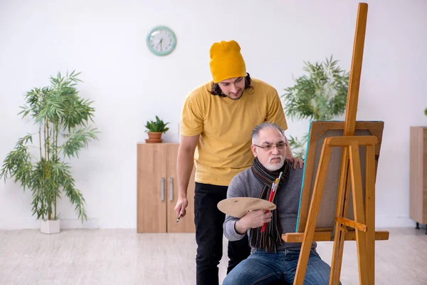 Old man taking lesson from young painter