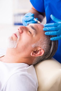 Yaşlı adam saç nakli için genç erkek doktoru ziyaret ediyor.