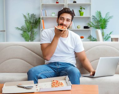 Pizza yiyen adam evde yemek yiyor, dinleniyor.