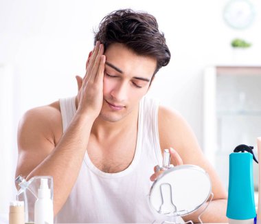 Genç yakışıklı adam aynaya bakıyor.